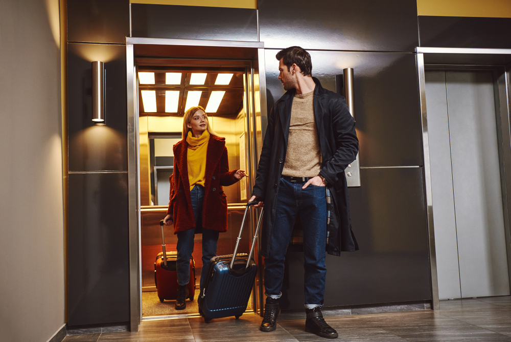 A man and woman are inside an elevator, illustrating a moment from British Transfers.